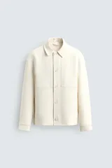 Sobrecamisa de diseño boxy fit en color blanco, confeccionada en tejido compacto. Cuenta con cuello solapa, manga larga con puño abotonado, bolsillos laterales invisibles en costura y cierre frontal con botonadura.