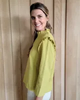 Blusa blanca de manga larga con cuello alto y volados en cuello y hombros.