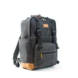 Mochila matera y porta notebook en tela canvas de color marrón, con diseño funcional que incluye bolsillo frontal con cierre, correas ajustables, manija superior y detalles de tiras de lona con hebillas metálicas.