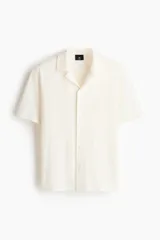 Camisa de manga corta color blanco hueso, de punto jacquard en mezcla de algodón, con cuello abierto y cierre frontal de botones.