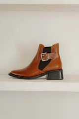 Botín negro de charol con punta cuadrada y hebilla metálica decorativa.