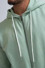 Chaqueta deportiva con cierre frontal completo, capucha con cordones ajustables y bolsillos tipo canguro, confeccionada en tejido de algodón en color verde menta.