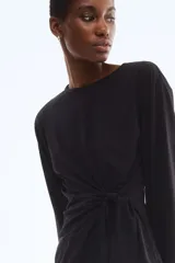Top negro de manga larga con escote redondo y un nudo ajustable en el lateral inferior.