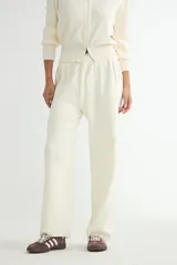 Conjunto de dos piezas tejido en color crema, compuesto por un cárdigan con cierre frontal completo y cuello alto, y pantalón de corte recto con cintura elástica.