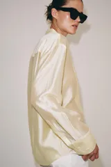 Camisa de mujer fluida de ZARA WOMAN COLLECTION, confeccionada en hilatura con mezcla de lyocell. Presenta escote en pico, manga larga con puños marcados y bajo asimétrico, con cierre frontal de botones ocultos.