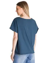 Remera de corte relajado color azul, con cuello redondo y mangas cortas con dobladillo. Presenta un estampado gráfico frontal con la inscripción Caterpillar A Tractor Company en tonos rojos y detalles botánicos.