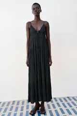 Vestido midi negro satinado con escote en pico, tirantes finos y detalle de lazada frontal. Presenta diseño de paneles fruncidos.