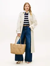 Cartera tote Tommy Hilfiger de color tostado, con acabado liso, dos asas superiores y cierre de cremallera. Cuenta con un compartimento principal, un bolsillo interior con cremallera y el logo metálico de la marca en relieve en la parte delantera.
