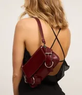 Cartera tipo baguette de material sintético efecto charol color bordó, con solapa frontal, detalles de hebillas metálicas decorativas en los laterales y asa corta ajustable.