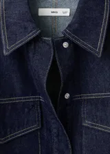 Camisa de jean de algodón con cuello camisero, cierre frontal de botones ocultos, mangas largas con puños abotonados y dos bolsillos delanteros con solapa.