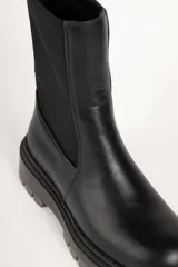 Bota corta negra de símil cuero, con punta redonda, laterales elastizados y suela tipo tractor de 5 cm de alto.