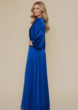 Vestido largo de fiesta confeccionado en satén azul brillante, con cuello redondo, mangas largas abullonadas con puños ajustados y falda con tajo lateral profundo.