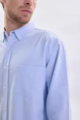 Camisa de manga larga confeccionada en tejido oxford color celeste, con cuello abotonado, cierre frontal de botones y bolsillo en el pecho.