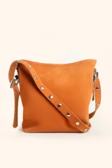 Cartera tipo balde de gamuza color suela, con correa ajustable decorada con tachas metálicas plateadas.