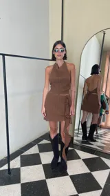 Pollera corta color marrón, confeccionada en crepé texturado con elasticidad. Presenta un diseño con volado lateral asimétrico que cae en cascada y detalles verticales en la textura de la tela.