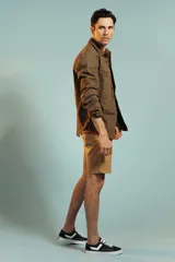 Bermuda de gabardina color tostado, de corte recto y largo por encima de la rodilla, con cierre y botón frontal.