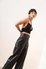 Pantalón de cuero sintético negro, de corte ancho, con bolsillos laterales y ruedo con dobladillo.