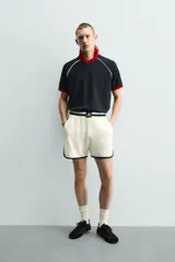 Polo de corte relajado confeccionado en tejido de algodón con estructura abierta. Presenta cuello polo con abertura frontal en V, mangas cortas tipo ranglán y acabados en rib a contraste en color rojo y blanco.