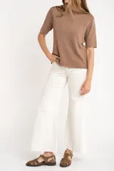 Sweater de tejido de punto fino en color arena, con cuello redondo y mangas cortas. Presenta un diseño minimalista con un pequeño detalle metálico en el ruedo.