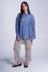 Camisa celeste de corte amplio, con cuello clásico, cierre frontal con botones, bolsillo en el pecho y mangas largas con puños abotonados.