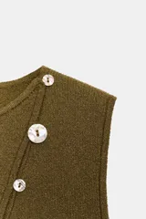 Top de punto color verde oliva, sin mangas, con cuello redondo y diseño ajustado. Presenta una hilera diagonal de botones nacarados en el frente.