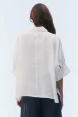 Camisa oversize blanca de lino, con corte cuadrado, mangas raglán cortas con puños anchos, aberturas laterales y cierre frontal de botones.