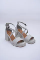 Sandalias de cuero color gris claro, con plataforma y taco cuadrado. Presentan tiras cruzadas sobre el empeine y pulsera con hebilla al tobillo.