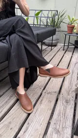 Zapatos tipo chelsea de cuero color marrón, con paneles elásticos laterales y suela plana de goma.