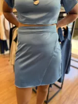 Conjunto de dos piezas color celeste satinado, compuesto por un top de escote en V con mangas cortas tipo volado y una falda corta tipo pareo con detalle de solapa cruzada.
