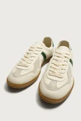Zapatillas de estilo retro para hombre, color blanco off-white con detalles en verde oscuro y suela de goma marrón estilo gum. Presenta cordones al tono, refuerzos en gamuza en la puntera y talón, y bandas laterales verdes en contraste.