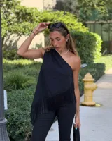 Blusa negra de un solo hombro con detalle de flecos en el ruedo asimétrico.