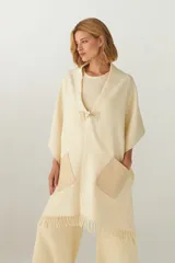 Chal de lana fina sin teñir con diseño de cuadros sutiles, cierre frontal con alamar y bolsillos de cuero metalizado. Presenta terminaciones con flecos en el ruedo y un calce estructurado en los hombros.