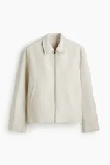 Campera de lino color beige, de corte regular con cuello clásico, cierre frontal y bolsillos laterales con ribete.