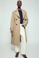 Trench largo de color negro con cuello de solapa, manga larga con trabillas ajustables y cierre frontal cruzado con doble botonadura. Cuenta con bolsillos delanteros de vivo, solapa cortavientos en el pecho y cinturón ajustable del mismo tejido.
