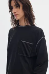 Remera de manga larga negra con bolsillo frontal en el pecho y costuras a la vista en contraste de color gris.