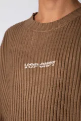 Sweater de punto acanalado con diseño de calce relajado, cuello redondo y mangas largas. Presenta una estampa gráfica pequeña en el centro del pecho y un parche con logo en el puño.