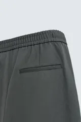 Pantalón regular fit color marrón oscuro, confeccionado en tejido con viscosa. Cuenta con cintura elástica, bolsillos delanteros y detalle de bolsillos traseros de vivo. El cierre frontal es con cremallera y botón.