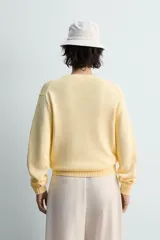 Jersey de punto color amarillo pálido, de corte relajado (relaxed fit), con cuello redondo y manga larga. Presenta acabados en rib en puños y bajo.