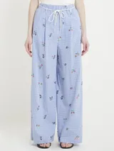 Pantalón de vestir de corte recto, con estampado de cuadros celestes y blancos, bordado de flores rojas y verdes, cintura alta con elástico y cordón decorativo.