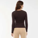 Camiseta de manga larga color marrón, confeccionada en tejido elástico, con cuello redondo y detalle de fruncido lateral con adorno metálico dorado. Presenta un corte asimétrico en el ruedo.