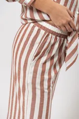 Pantalón largo de lino a rayas verticales color marrón y blanco, con cintura elástica y bolsillos laterales.