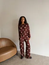 Conjunto de dos piezas compuesto por buzo de corte holgado con cuello redondo y mangas largas, y pantalón de corte recto y tiro alto. Ambas prendas están confeccionadas en lanilla color marrón con estampado de lunares blancos.