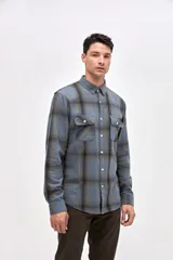 Sobrecamisa de algodón con diseño a cuadros en tonos azules y grises. Presenta cuello clásico, cierre frontal con botones y dos bolsillos en el pecho con solapa.