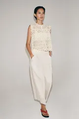 Blusa sin mangas confeccionada en tejido tipo crochet con diseño geométrico calado, cuello redondo y cierre frontal con botones.