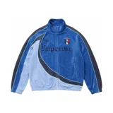 Campera deportiva de terciopelo Supreme x Umbro en color azul, con cuello alto, cierre frontal completo y bolsillos laterales. Cuenta con paneles en distintos tonos de azul y celeste, líneas curvas decorativas, y los logotipos de Umbro y Supreme bordados en el pecho junto con el escudo del Club Nacional de Football.