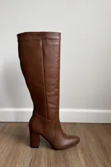 Bota de caña alta confeccionada en cuero vacuno color suela, con taco cuadrado y punta redondeada.