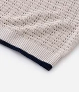 Camisa polo de manga corta, color beige claro, con textura de tejido abierto tipo ganchillo. Posee cuello y ribetes en las mangas en color azul marino.