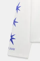 Remera de manga larga y corte oversize, color blanco, con cuello redondo. Presenta un estampado gráfico en color azul en el pecho y a lo largo de la manga derecha.