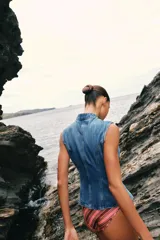 Top de denim sin mangas, con cuello mao y cierre frontal cruzado con trabillas y botones metálicos.