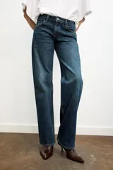 Jeans de mezclilla azul oscuro con efecto lavado, tiro bajo y pierna ancha extra larga. Modelo de cinco bolsillos con cierre frontal de cremallera y botón metálico.